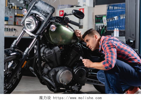 一个在维修摩托的男人车间摩托车诊断时，穿着格子衬衫的年轻机械师拿着套筒扳手